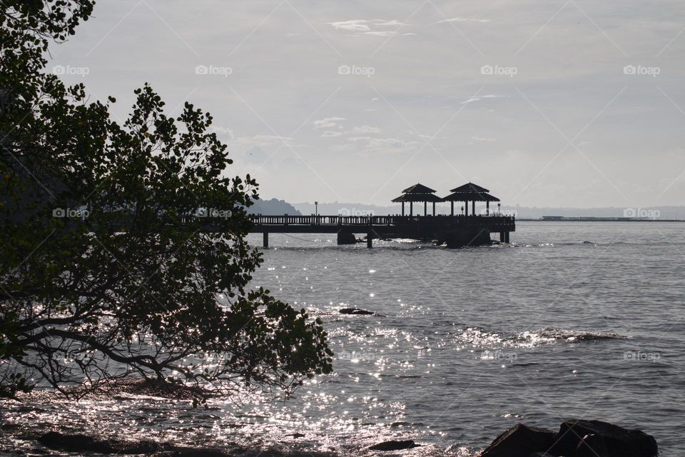 Sunlight sparkling on the water near the island and beach of Pulau Ubin in Singapore with the jetty.