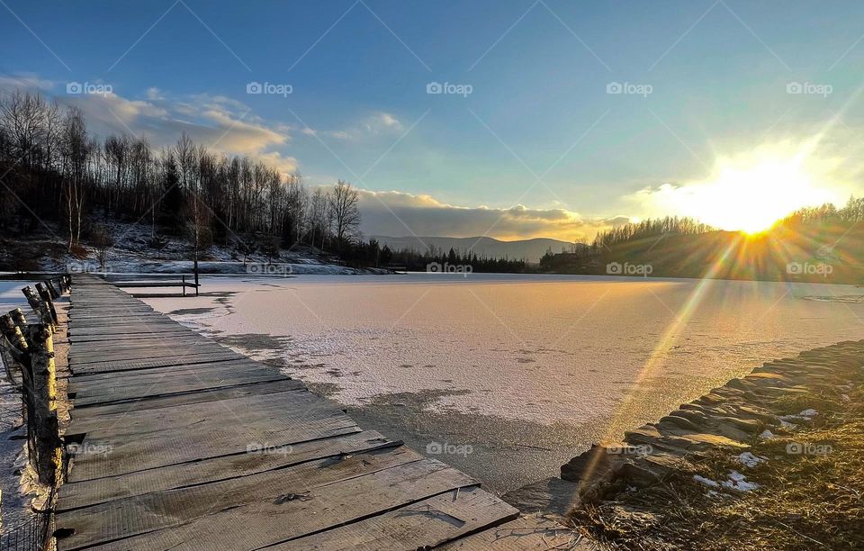 Winter sunset on the frozen lake with wooden bridge in the Carpathian mountains 