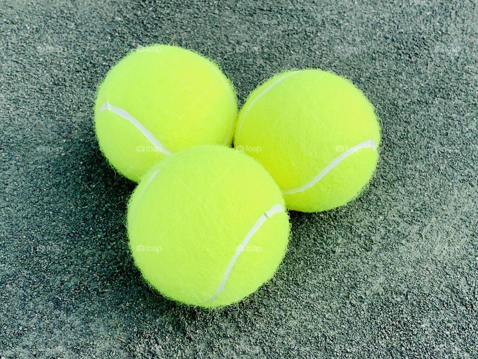 Three tennis balls on the clay court.