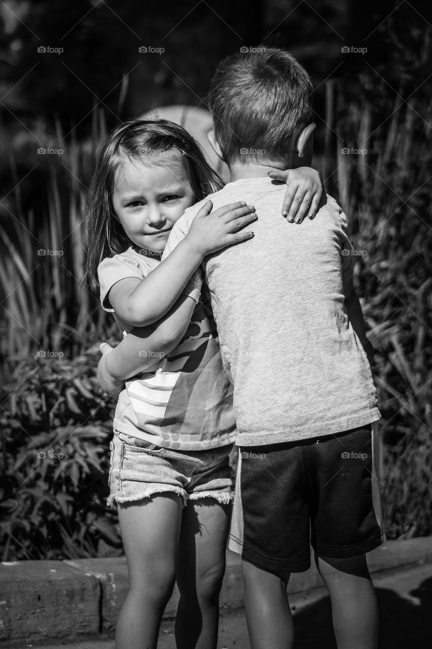 Black and white photo of two young toddlers hugging at the lake on a summer day 