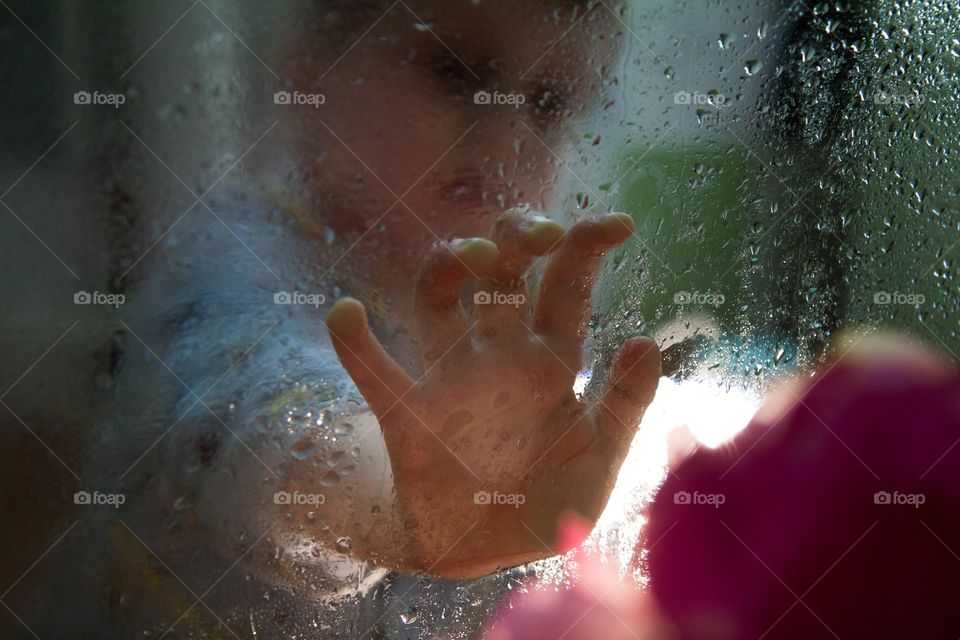 sad boy touching wet glass
