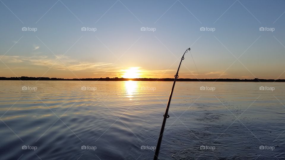 Fishing on a lake at sunrise with a beautiful reflection of the sun on the water