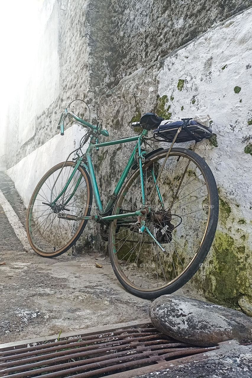 an old green bicycle parked next to a rough and old stone wall