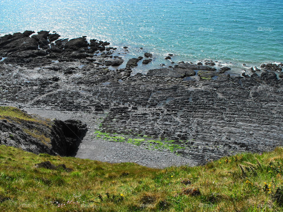 An eroded beach as seen from a grass covered cliff