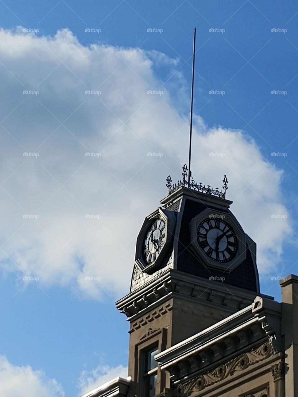 Pictured is a clock tower atop a 19th century building with a cloud filled sky
