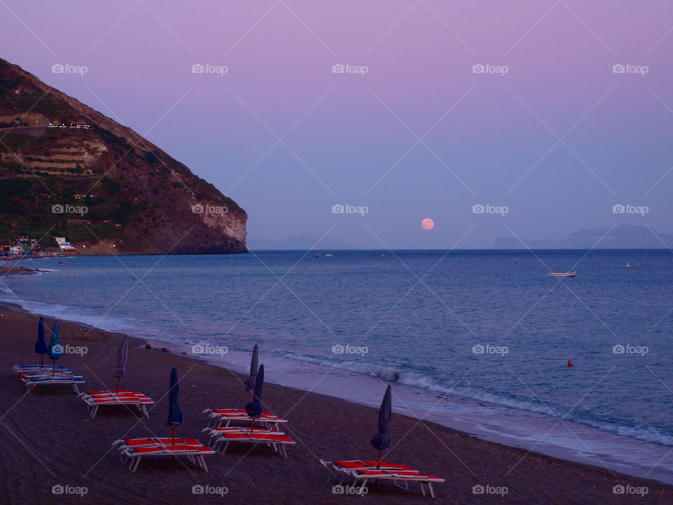 sunset on the beach with the moon on the distance