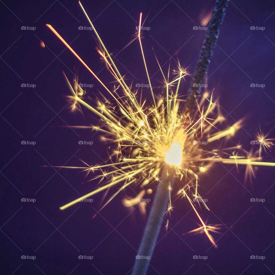 A lit and sizzling sparkler against a dark purple background 