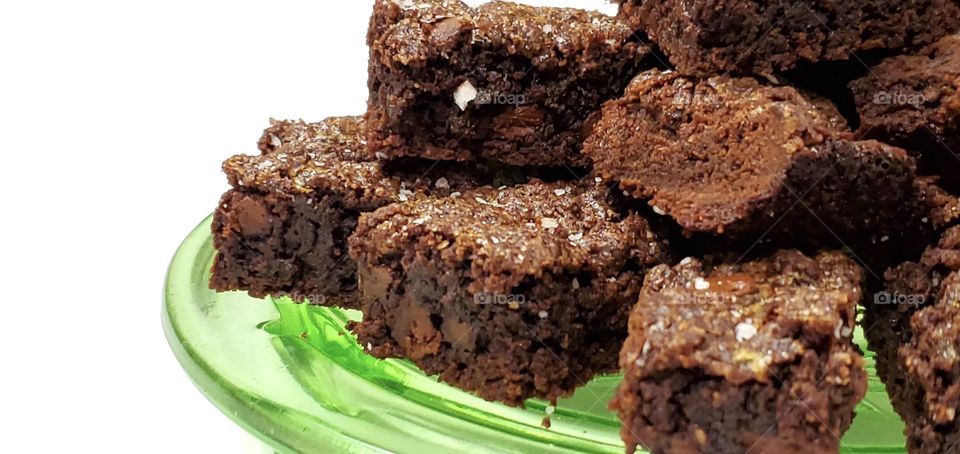 Chocolate brownies on a green glass plate with a white background 