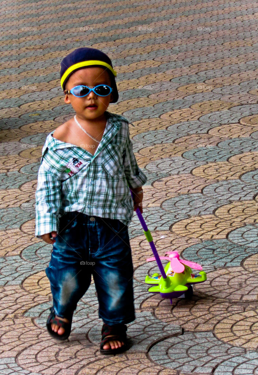 Little boy wearing sunglasses playing with toy on sidewalk