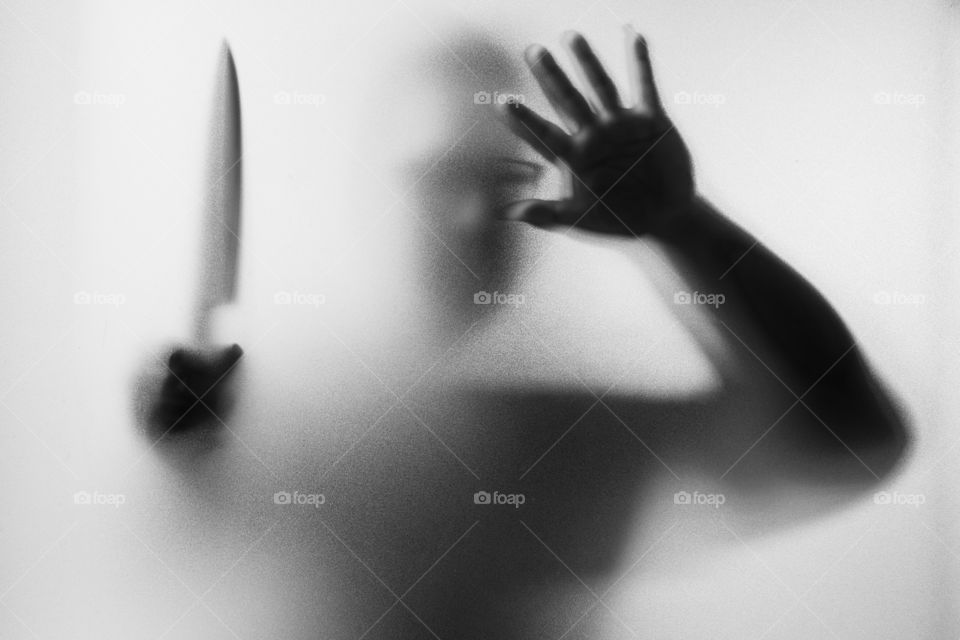 Horror Murderer. Dangerous man behind the frosted glass with a knife on his hand.Halloween background.Black and white picture