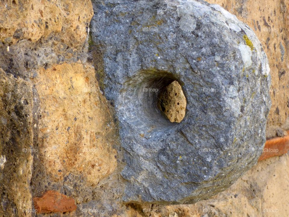 Round stone with a hole in the middle set into a stone wall. Made by the Etruscans in Civita di Bagnoregio, Italy.
