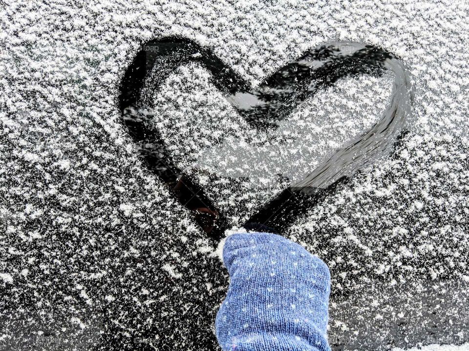 hand with Mitten on drawing a heart on a snowy window