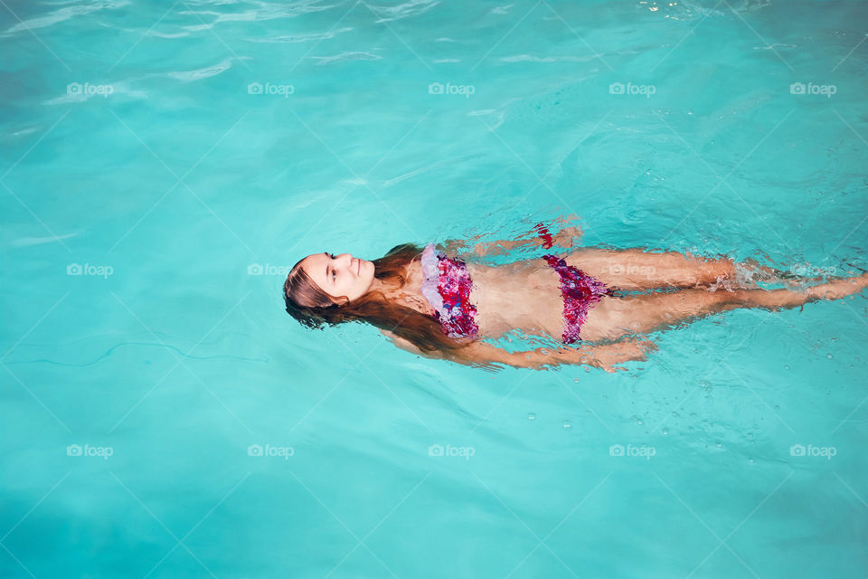 Young woman swimming and relaxing in swimming pool. Candid people, real moments, authentic situations