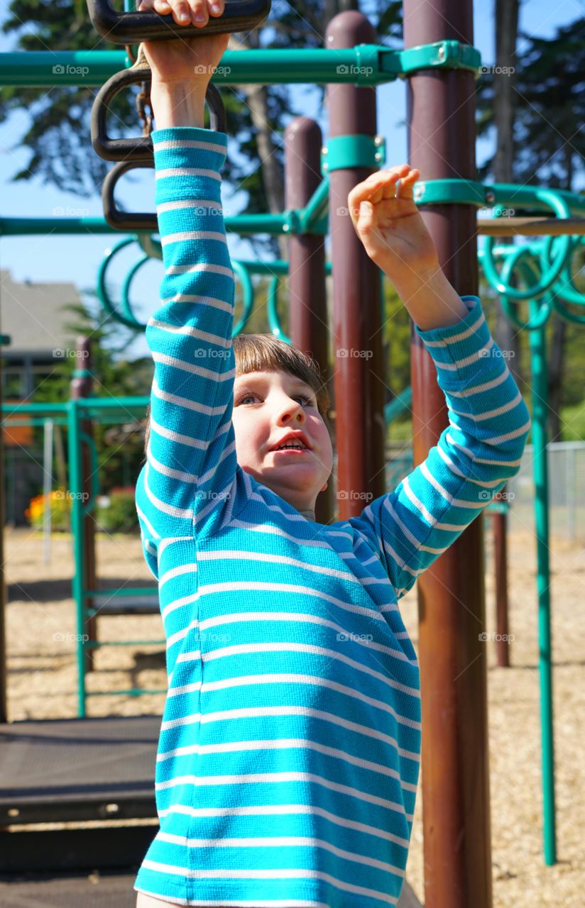 Young Boy Swinging On Monkey Bars