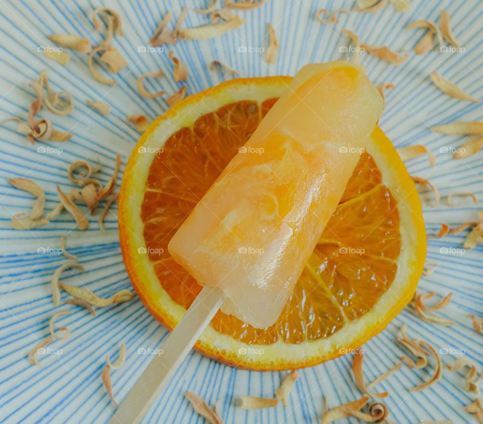 Orange ice lolly on a blue plate with orange slice and dried peel