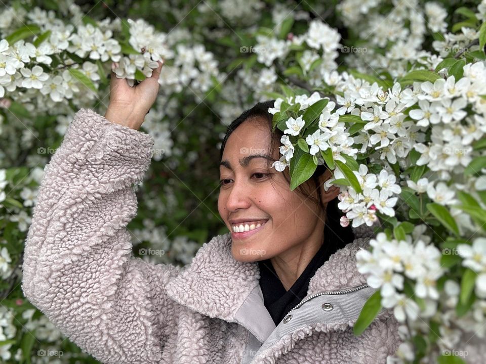 Happy woman enjoying the beauty of spring. Hand raised holding the branches of the flowering tree. 