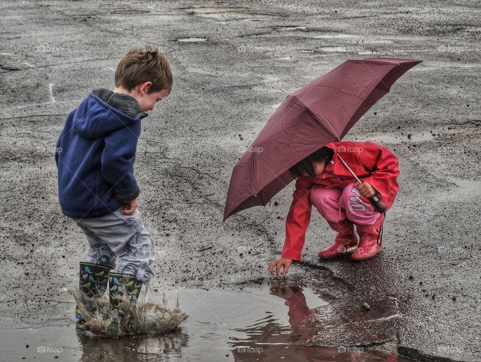 Umbrella Fun In The Rain. Young Boy And Girl Playing In Rain Puddles
