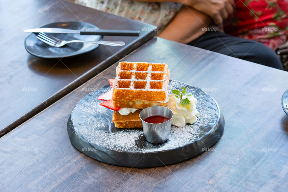 Waffle Strawerry fresh cream in the black plate on wooden table.