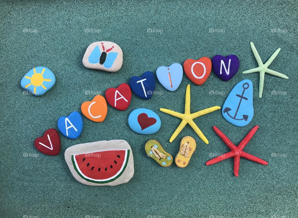 Vacation text with multicolored stones composition over green sand 