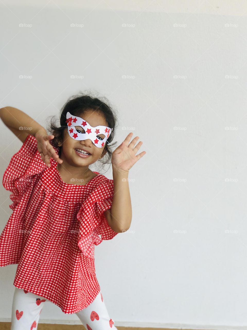 A cute girl having fun with hand made eye mask with red and white combination.