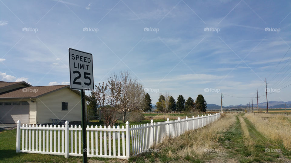 25 Mile per hour speed limit sign in front of a yellow house with a white picket fence