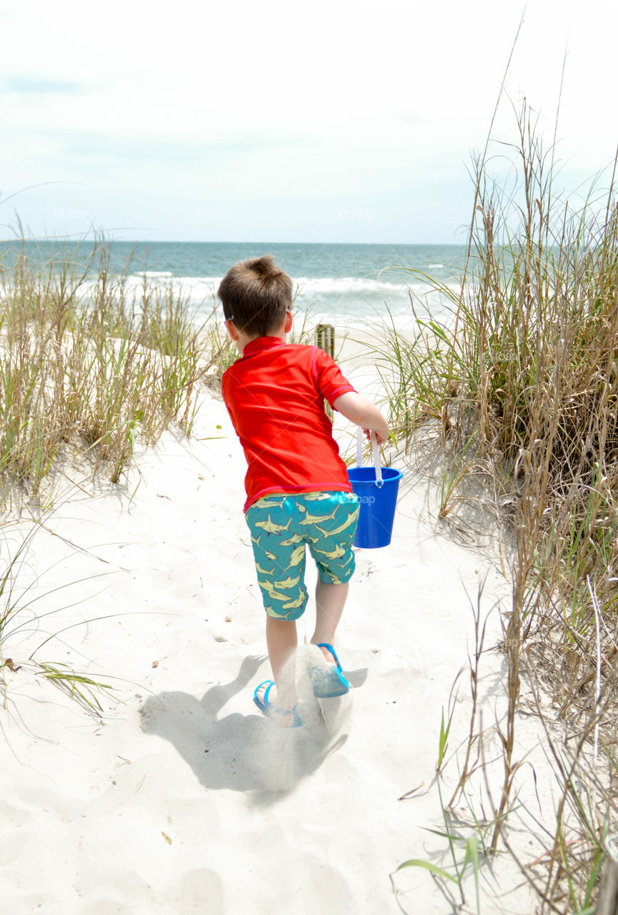 Young boy running through sand dunes on the beach to get to the ocean