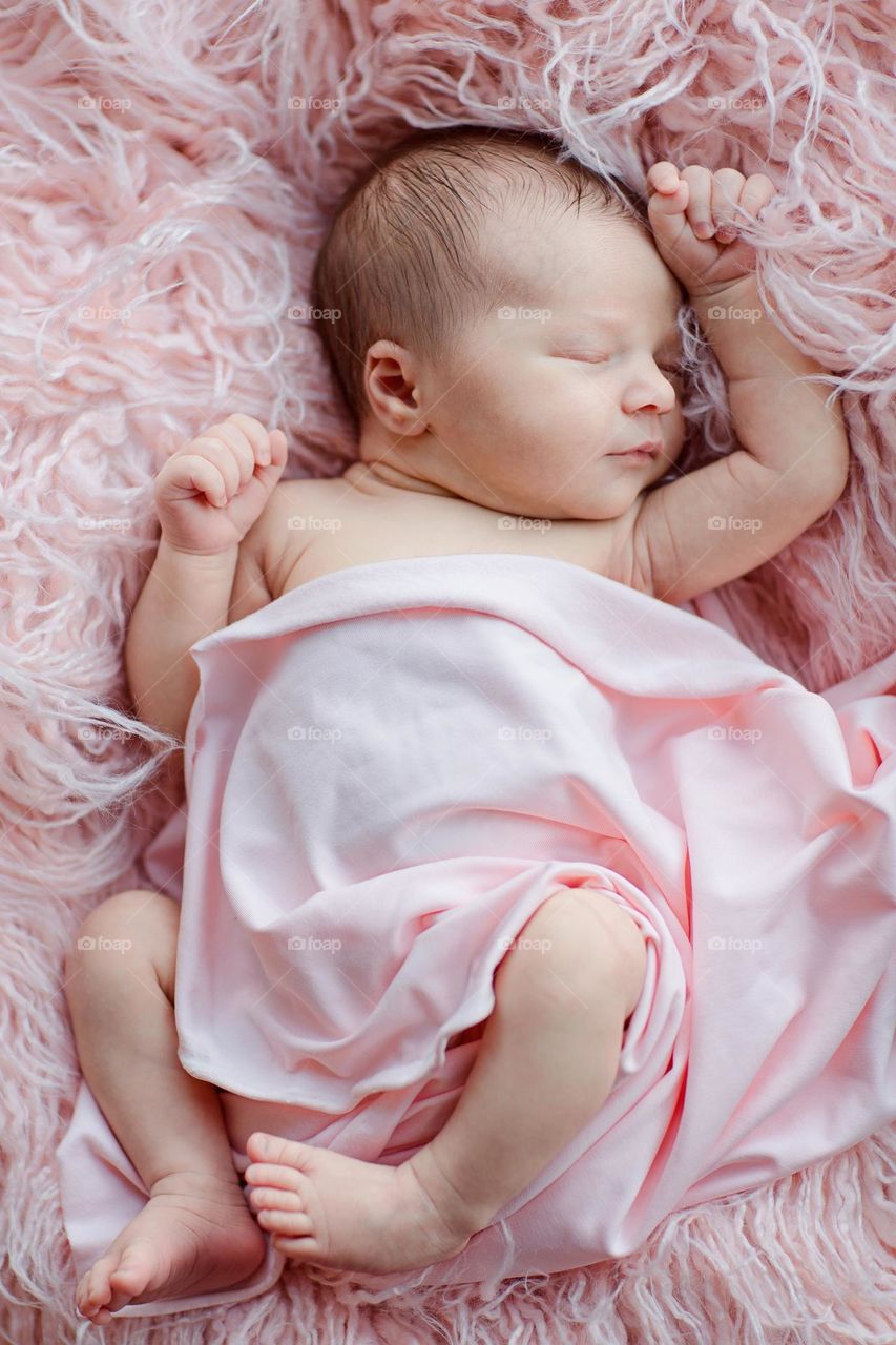 Adorable newborn baby girl is sleeping on pink furry blanket 