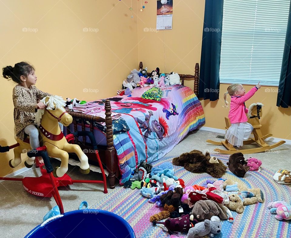 Two toddlers riding their horses in a bedroom, playing with stuffed animals in the bedroom, toddlers playing cowgirls 