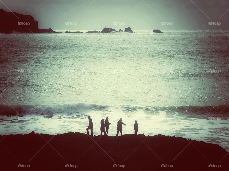Cliff Top Adventurers. Five people climbing and walking on cliff tops with the rolling waves of the ocean behind them.