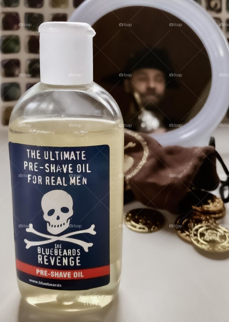 Pirate beard oil, displayed with some booty and a pirate can be seen in the mirror, scratching his beard with his hook hand