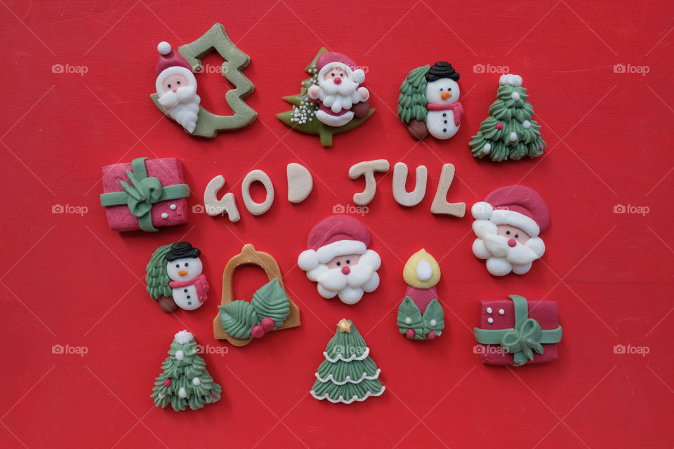 Creative swedish and norwegian Merry Christmas, God Jul, with wooden letters and marzipan Christmas symbols over red color background