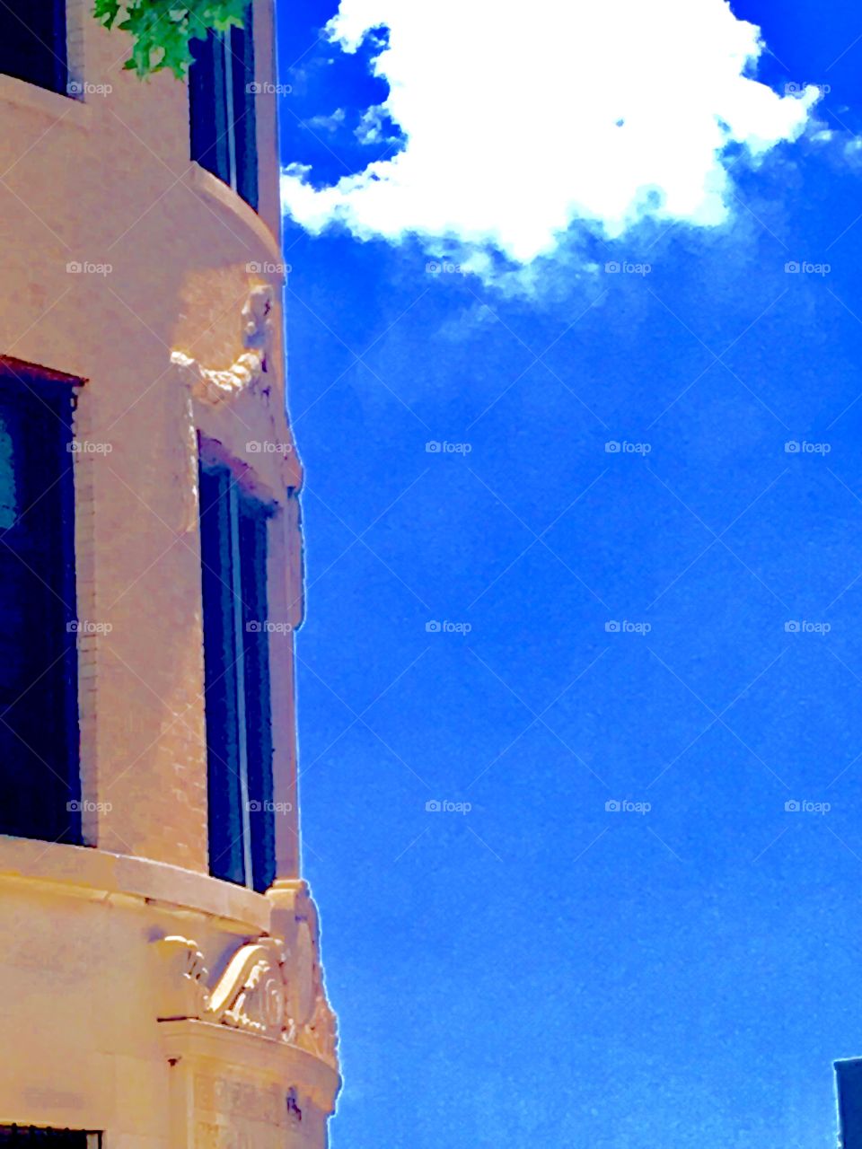 Clear blue skies with the exception of one white cloud are seen behind this unusual round shaped building with ornamentation by the windows on Fulton Street in Brooklyn, NY. The photo was taken in the summer of the year 2020. Hypnotic Productions