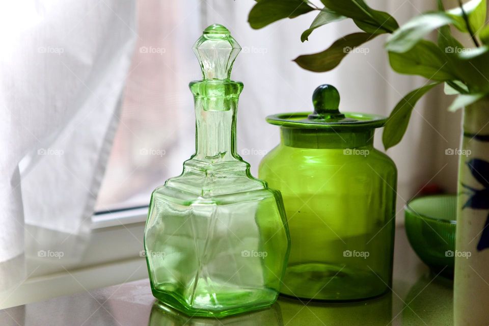 Antique vintage green glass containers, a beverage decanter and lidded glass ginger jar, still life, on countertop in front of window, conceptual collectibles, interior design display, home accessories