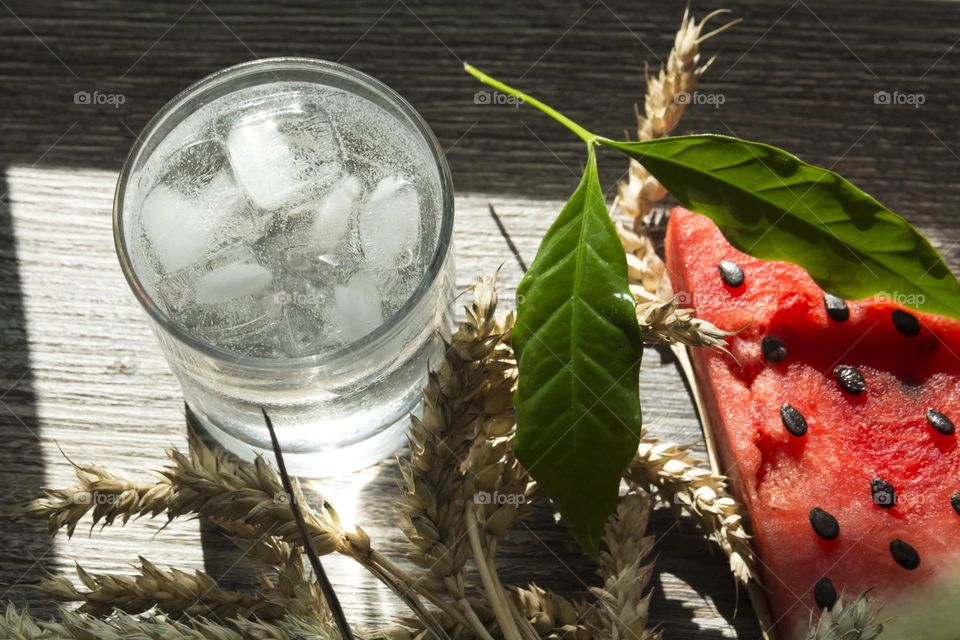 Cold, transparent drink with ice in a glass glass with summer snacks on a wooden background.