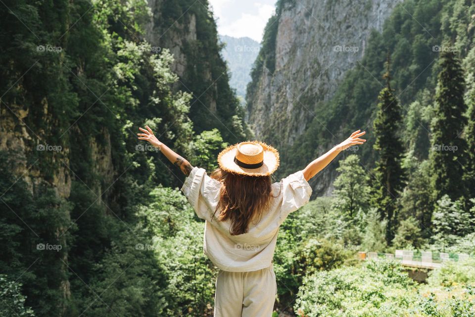 Young woman traveler with long blonde hair in straw hat looks at beautiful view of mountains, people from behind