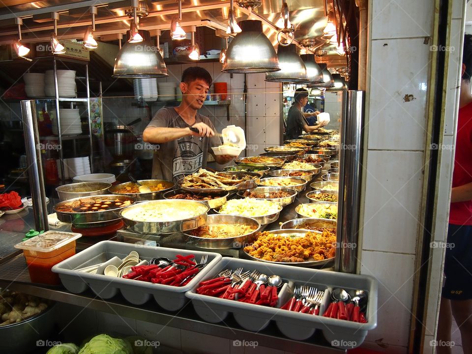 a man selling a variety of cooked food at a hawker