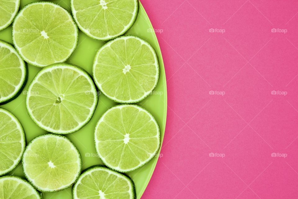 Minimalistic flat lay of lime slices on a green plate against a bright pink background