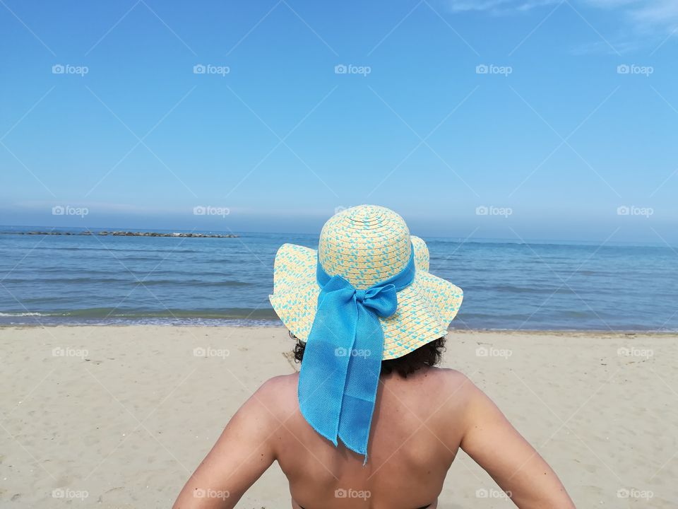 Woman with straw hat looks at the sea