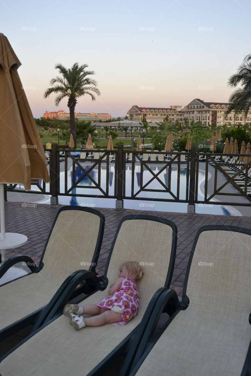 Little girl that is on vacation with her family in Turkey has fallen asleep on a lounger by the pool.