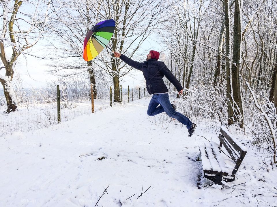 Man flying mid-air holding umbrella in winter