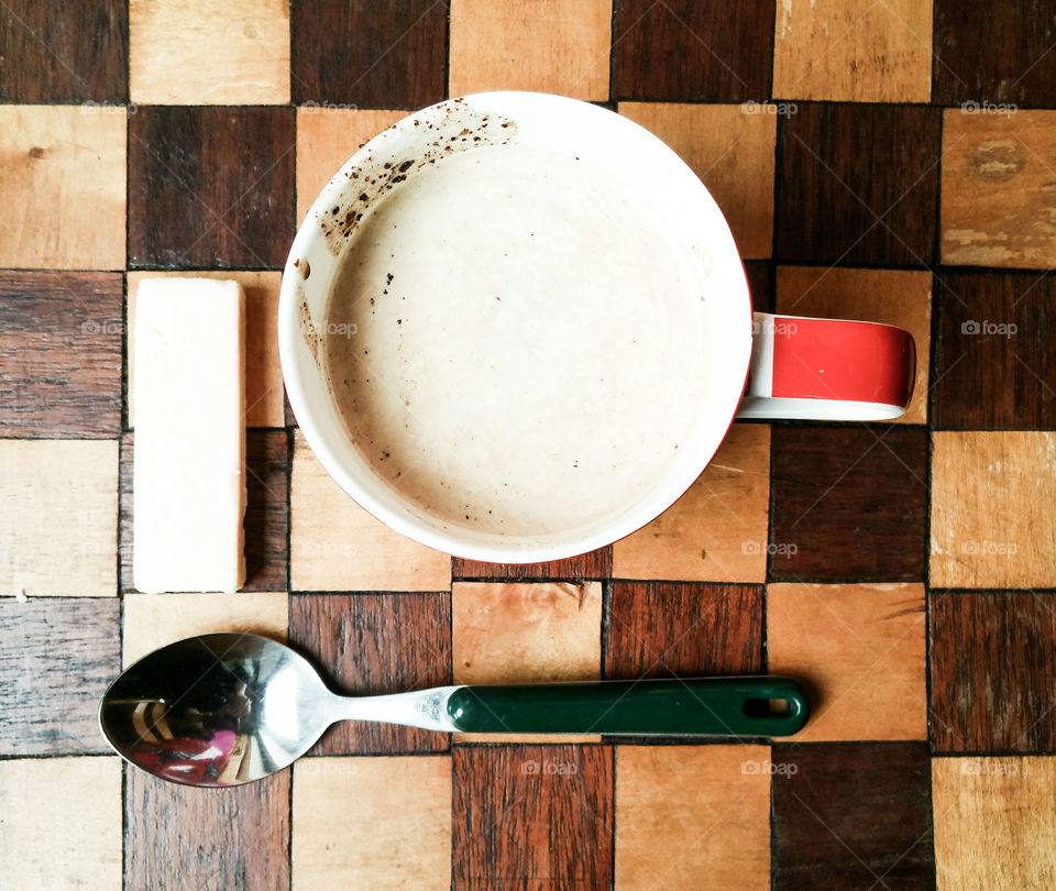 A cup of creamy coffee and a piece of cheese served on a chess board