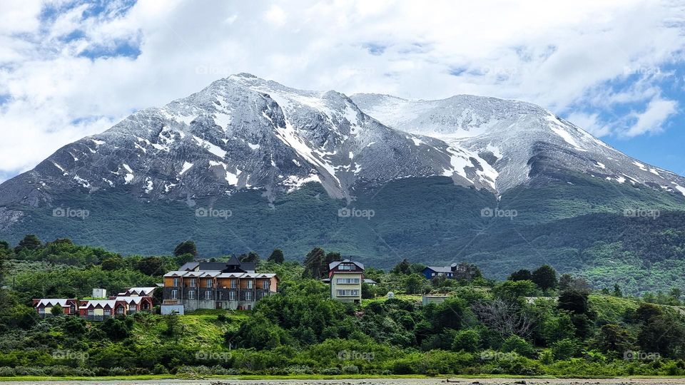 snowy mountains, green vegetation, cloudy sky