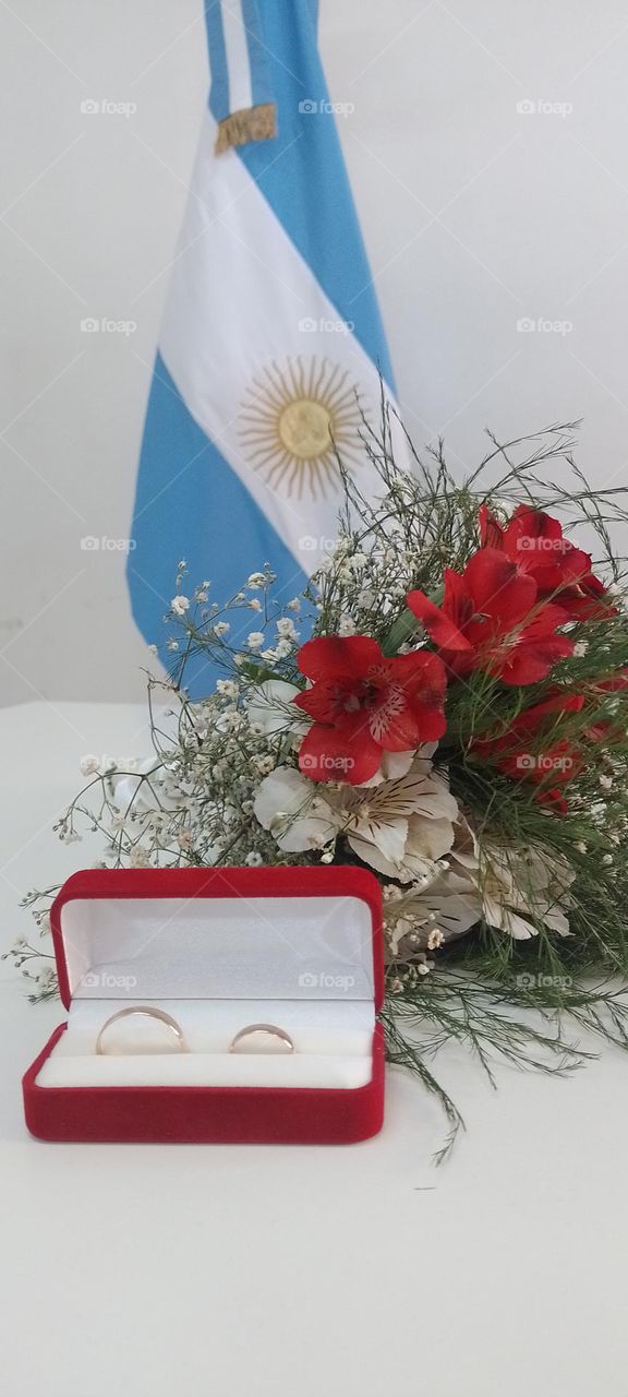 anillos de boda flores y una bandera de argentina de fondo