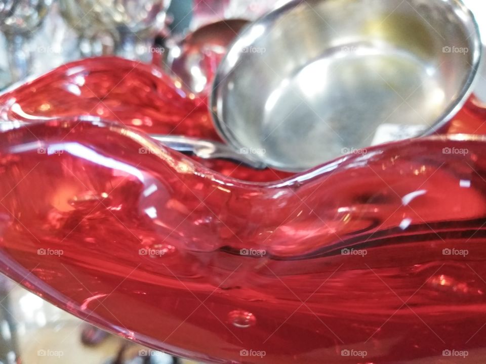 Contrast of a scarlet red glass serving dish and a silver serving ladle.