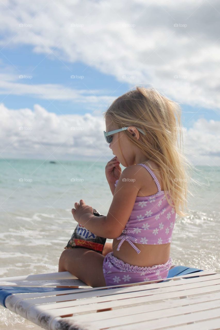 cute little girl eating a snack at the beach