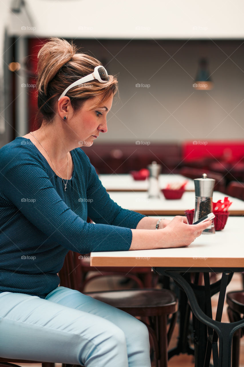 Young woman using mobile phone sitting by a table in cafe