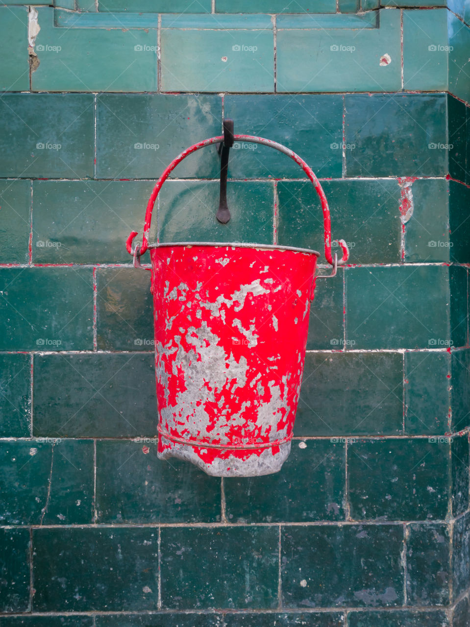 Old red bucket on green tiled wall.