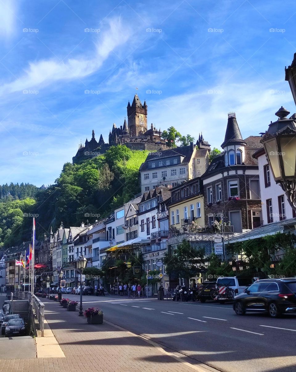 An amazing photograph of an empty beautiful street, its colourful houses and the stunning castle on a hill above /The beauty of the little german village called Cochem and its signature fortress looming over it /A colourful architectural design