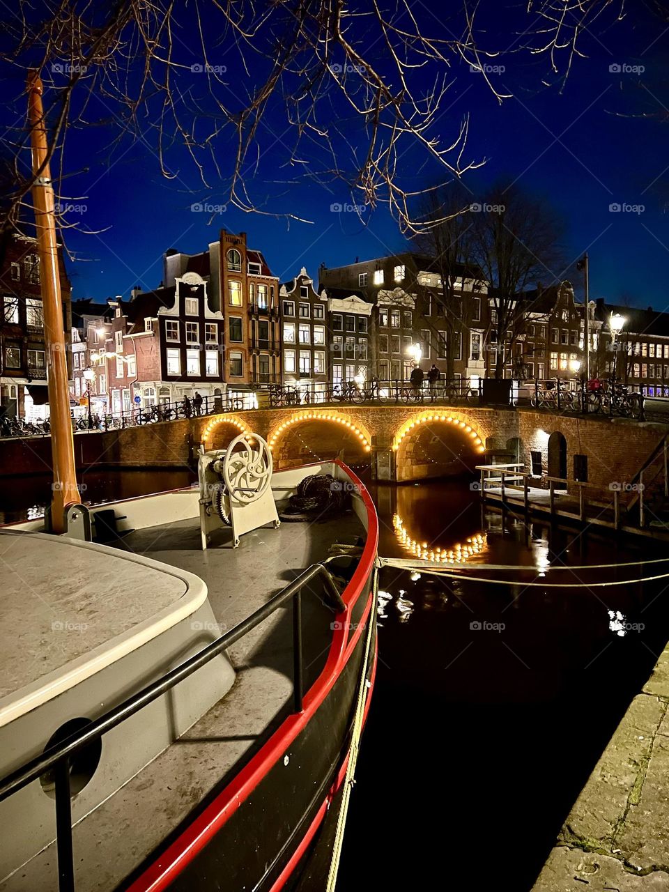The photo shows traditional Dutch wooden shoes used as tulip pots, placed next to a canal with houses in Amsterdam.