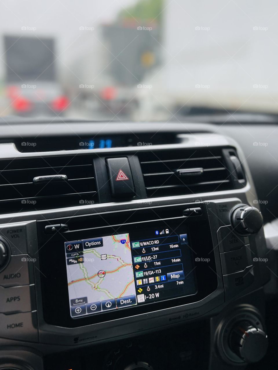 View from inside moving car. Focus on dashboard navigation system with vehicles, taillights and roadway in background